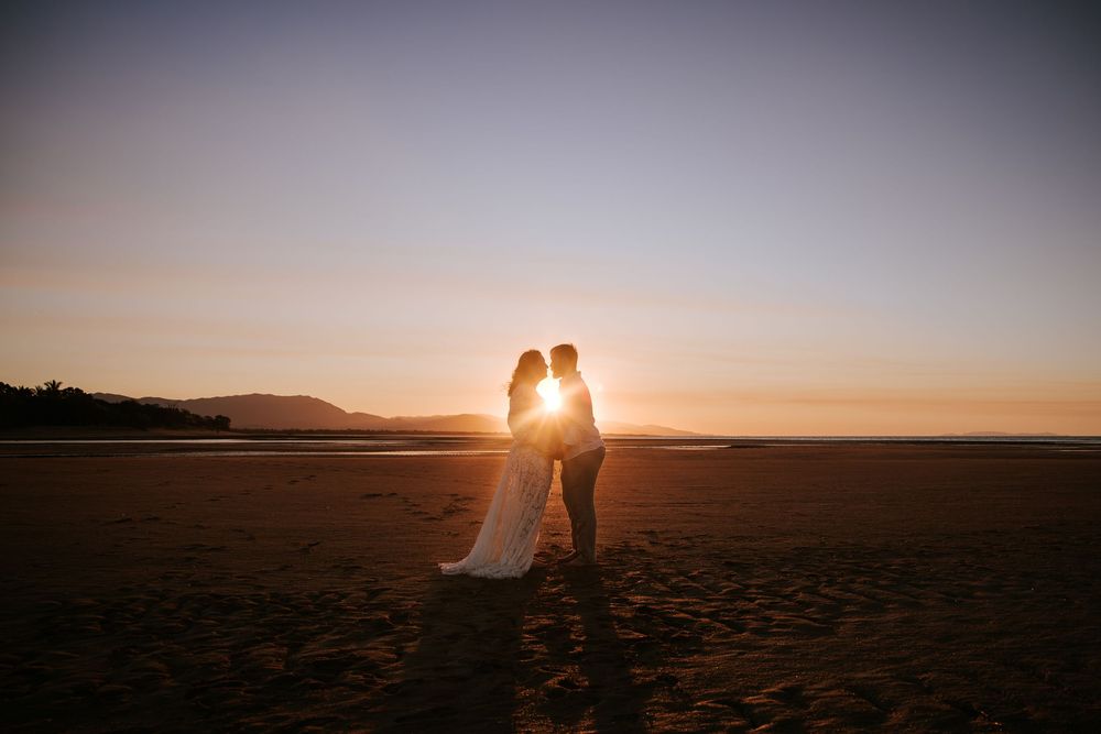 A couple in silhouette embraces on a beach at sunset creating a romantic golden hour moment.