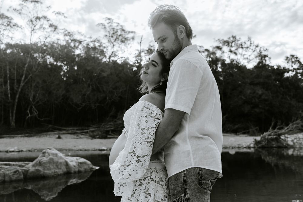A couple embraces during an intimate outdoor maternity photoshoot near a lake.