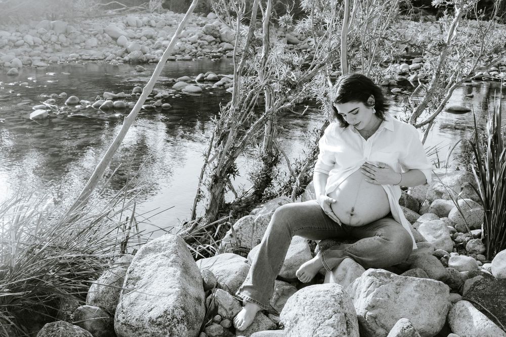 A vintage black and white photograph shows someone relaxing on rocks beside a tranquil stream.
