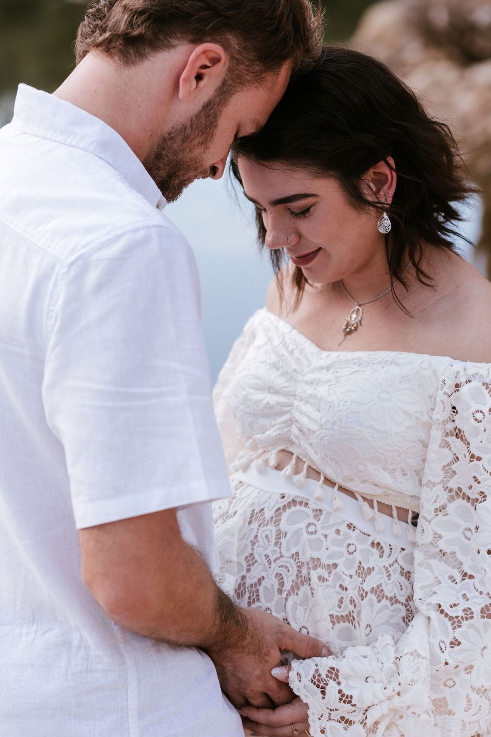 A romantic wedding couple embraces in white attire against a soft blurred background.
