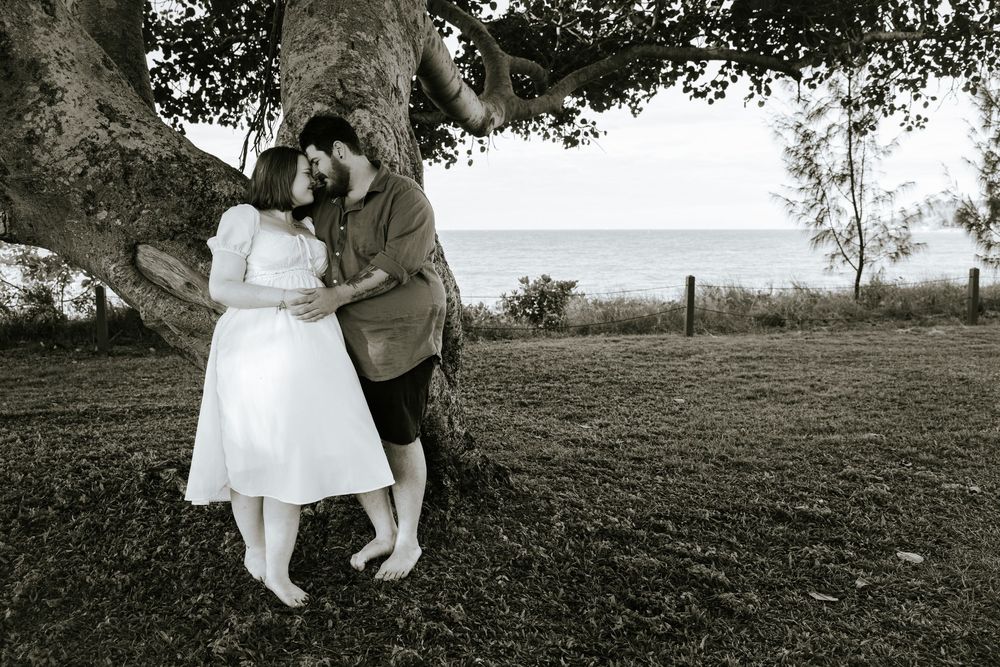 A romantic black and white photo series showing a couple sitting and embracing under trees in a park setting.