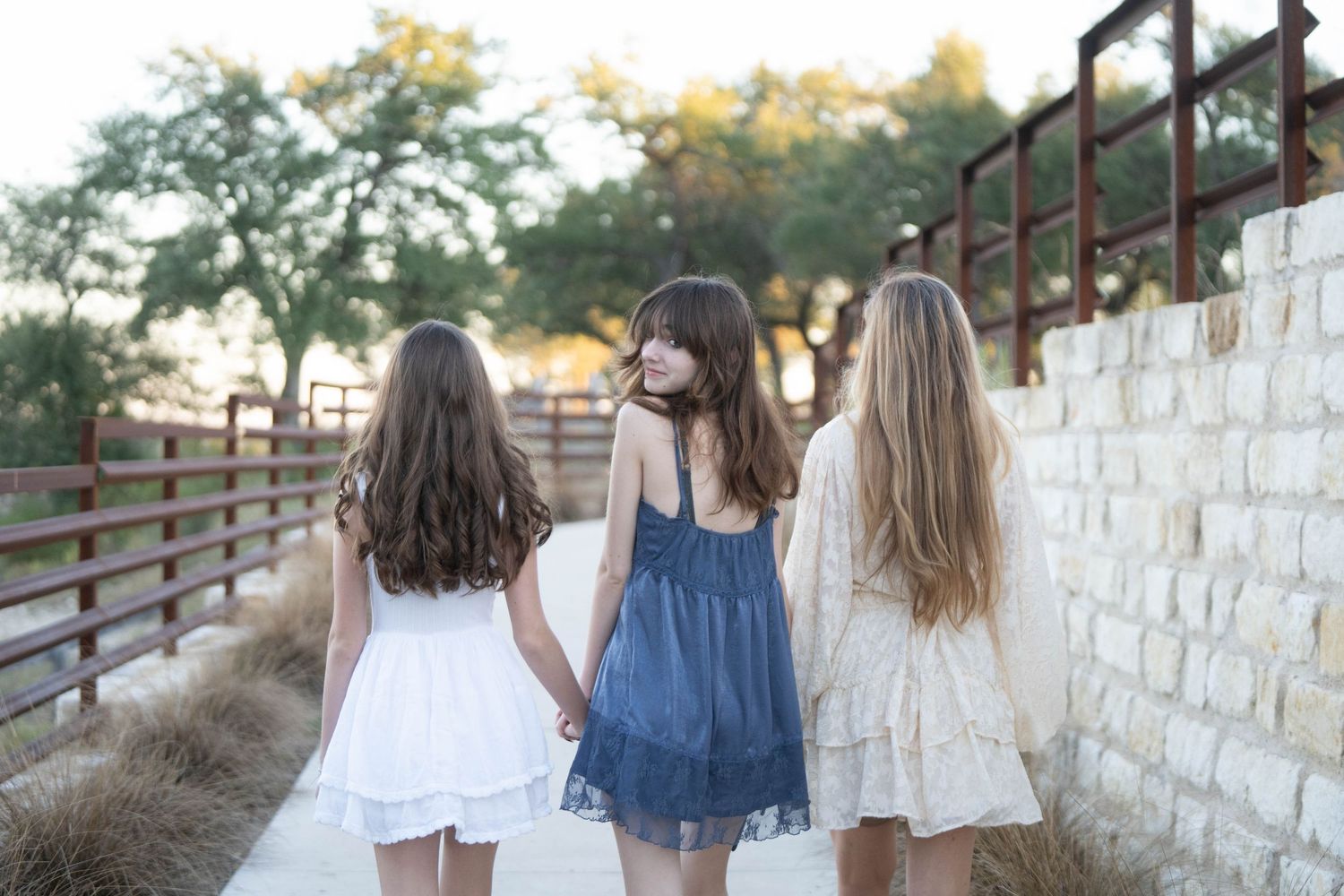 Group of friends walking along a stone wall path while holding hands on a sunny autumn afternoon.