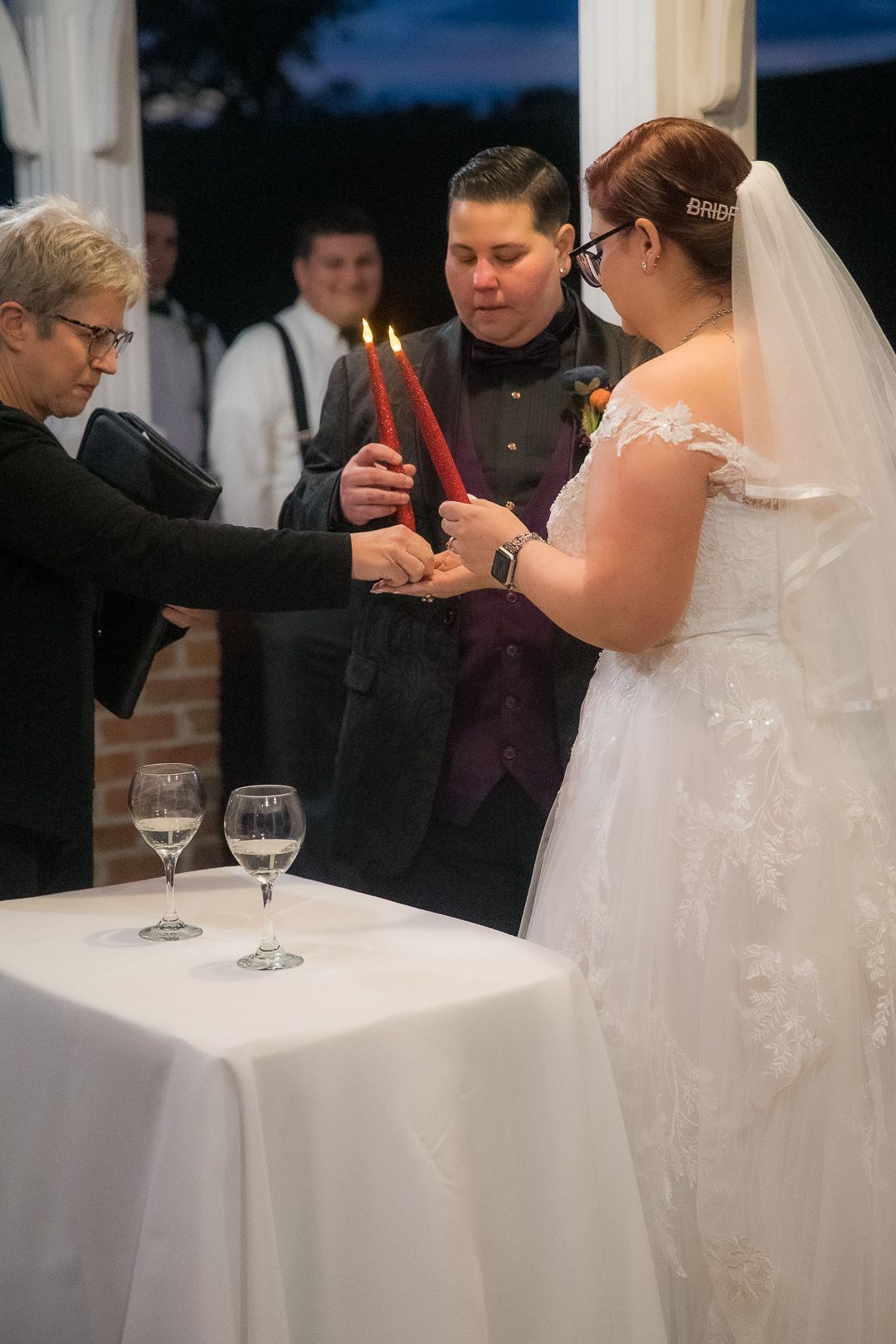 Wedding couple signs documents at a table with wine glasses during an indoor ceremony.