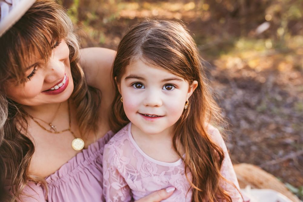 Two children in pink dresses sit together and laugh during an outdoor autumn photoshoot.