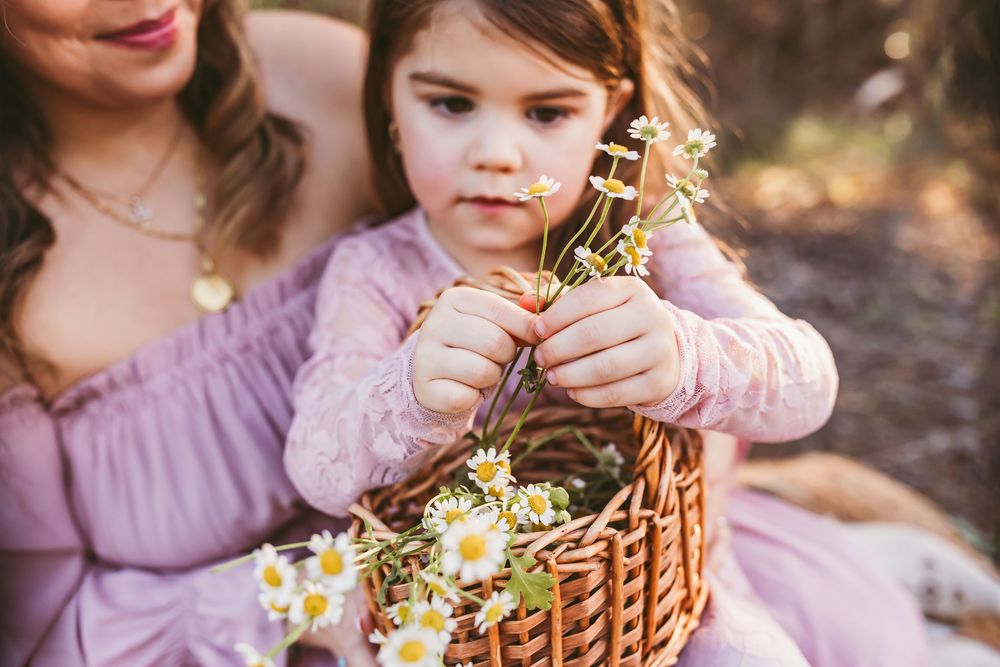 Mother and daughter in matching pink dresses gather flowers in a sunlit garden.