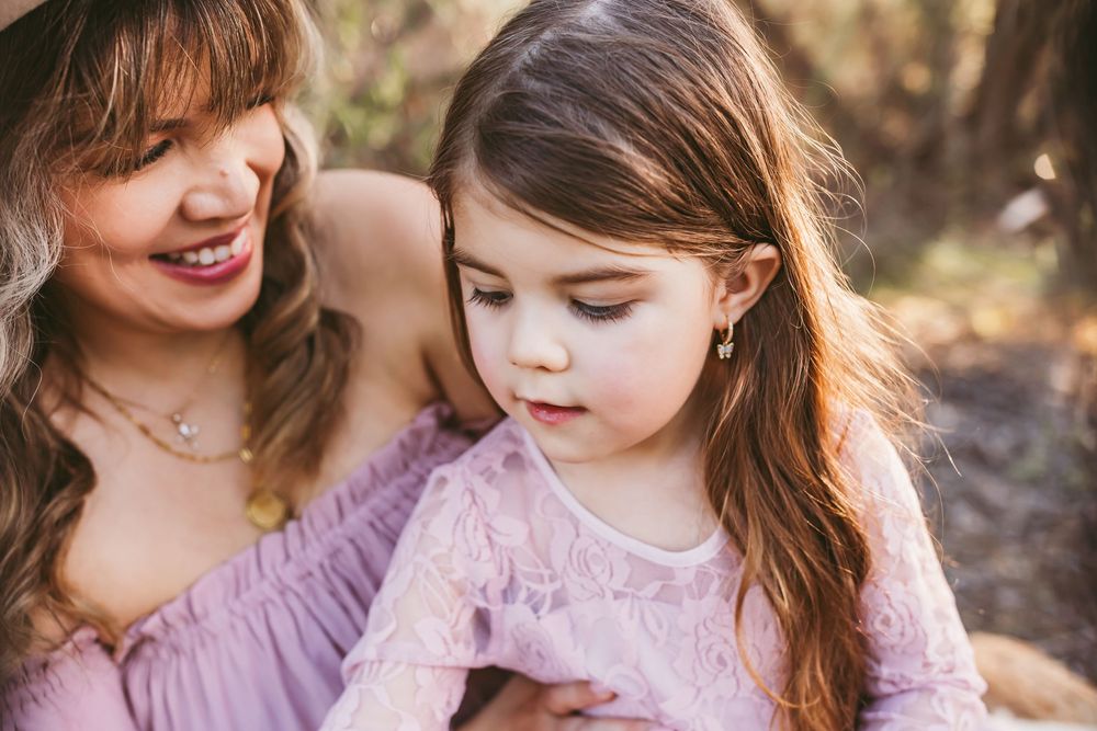 A tender moment captured outdoors between two people wearing purple and pink tones in natural sunlight.