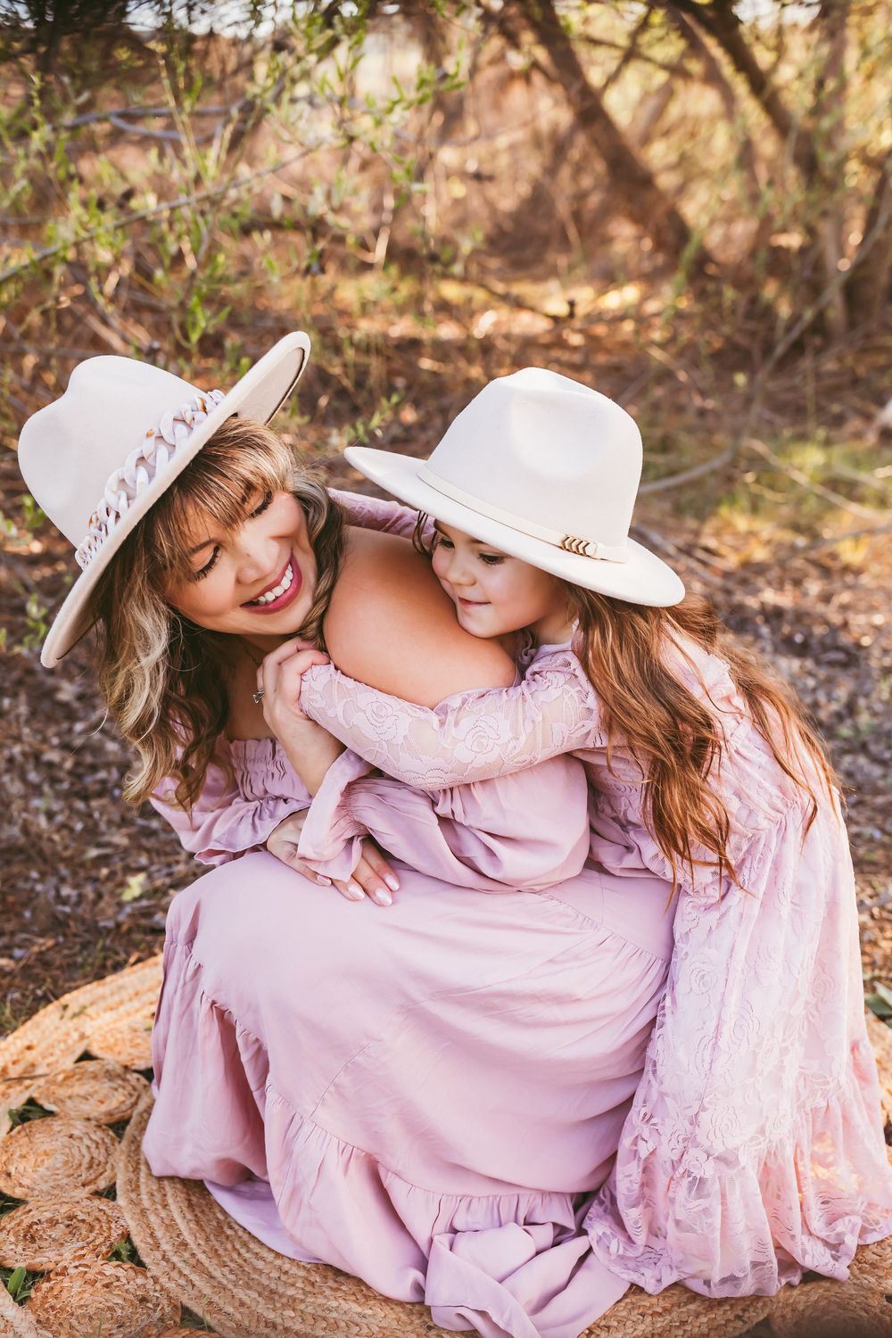 Tender bonding moment captured outdoors with matching pink dresses and white cowboy hats on a picnic blanket.