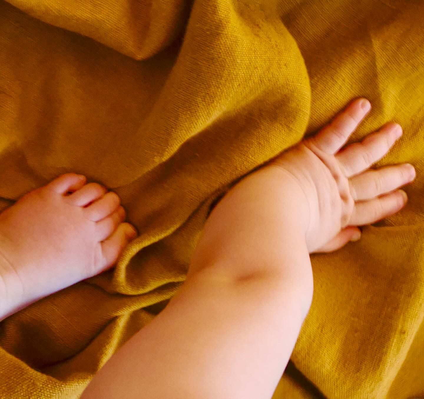 Détails des mains et pieds d’un bébé sur un tissu chaleureux pendant une séance photo bébé lifestyle par WA Visuel photographe en Provence.