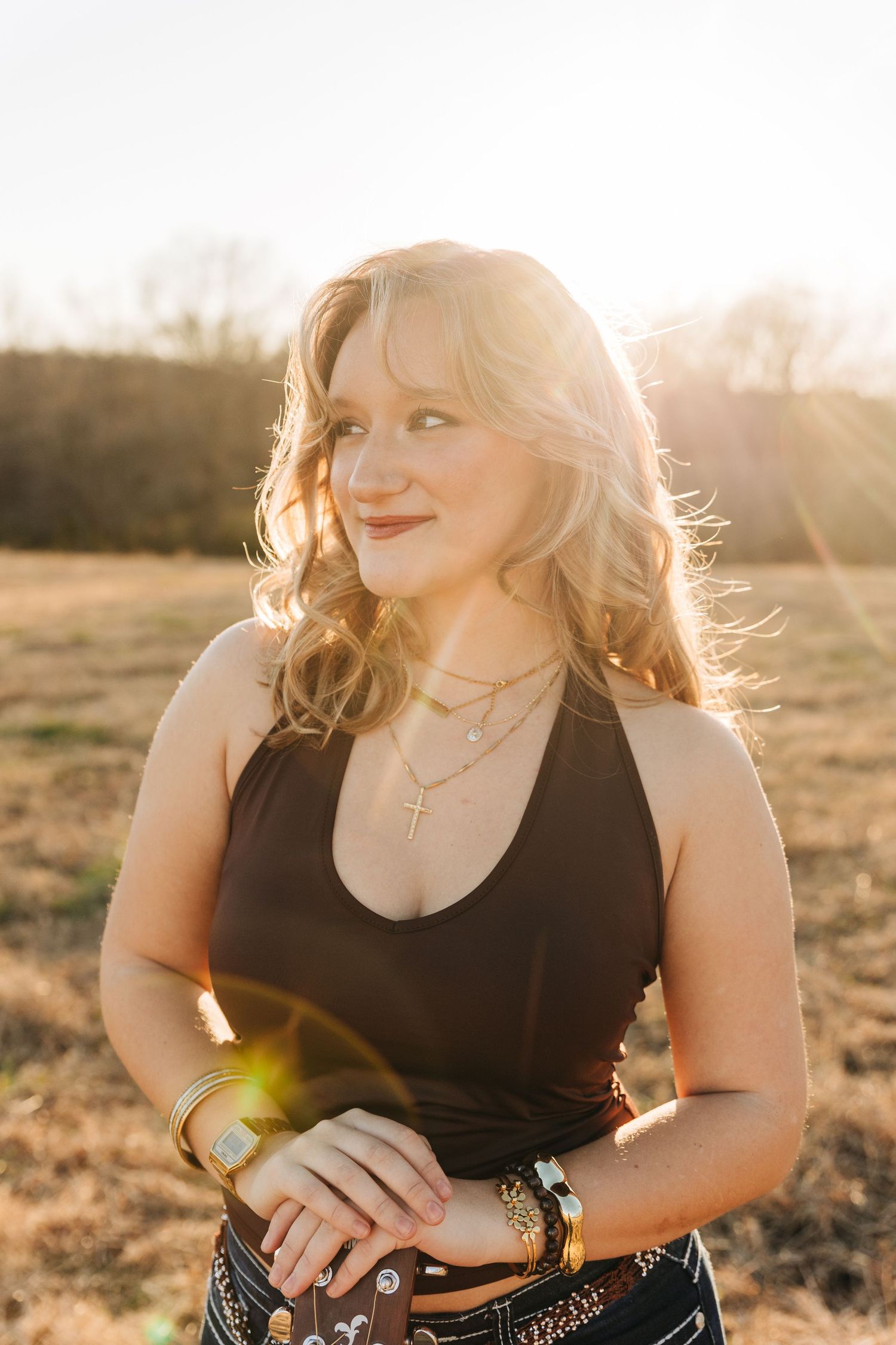 A person in a black top poses outdoors during golden hour sunset with sun flares creating a dreamy atmosphere.