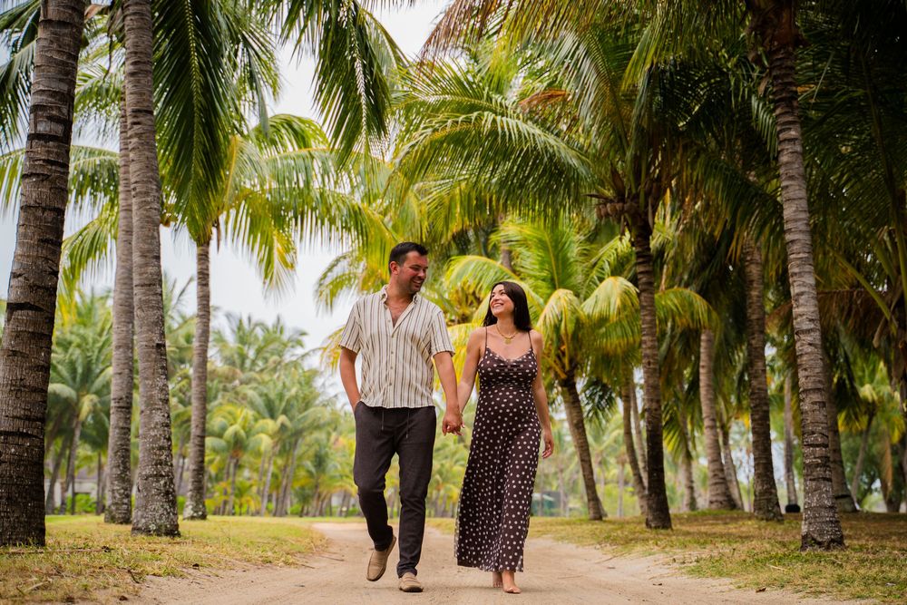 A couple strolls hand in hand through a tropical palm tree lined path.