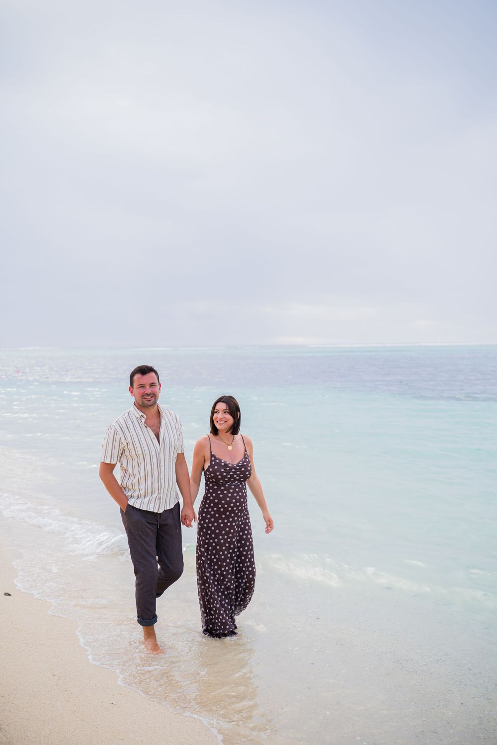 A couple walks together in the shallow turquoise waters of a tropical beach.