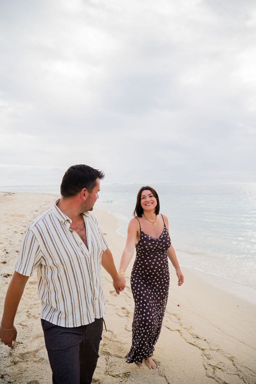 A couple laughs while walking along a pristine sandy beach with turquoise waters.