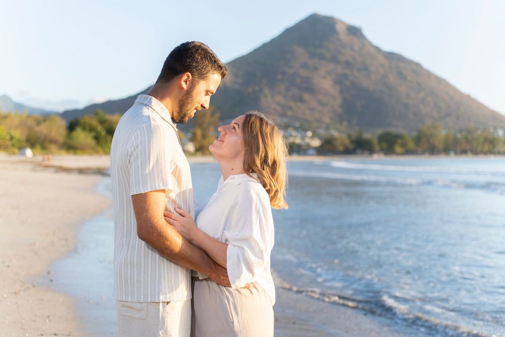 A couple embraces on a scenic beach with mountains in the background.