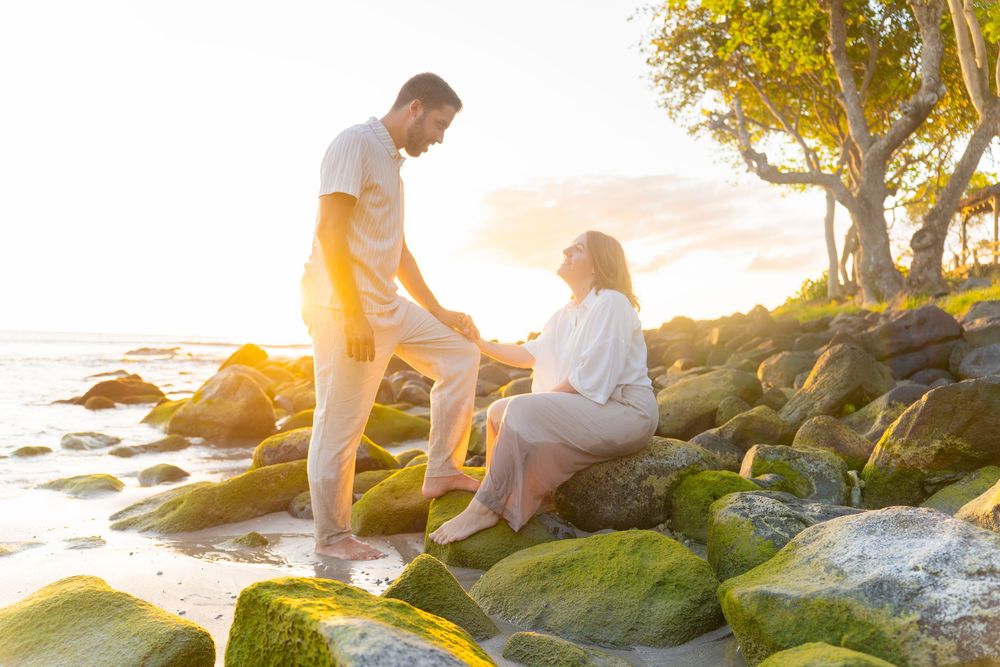 A couple sits together on rocky coastal formations at golden hour.
