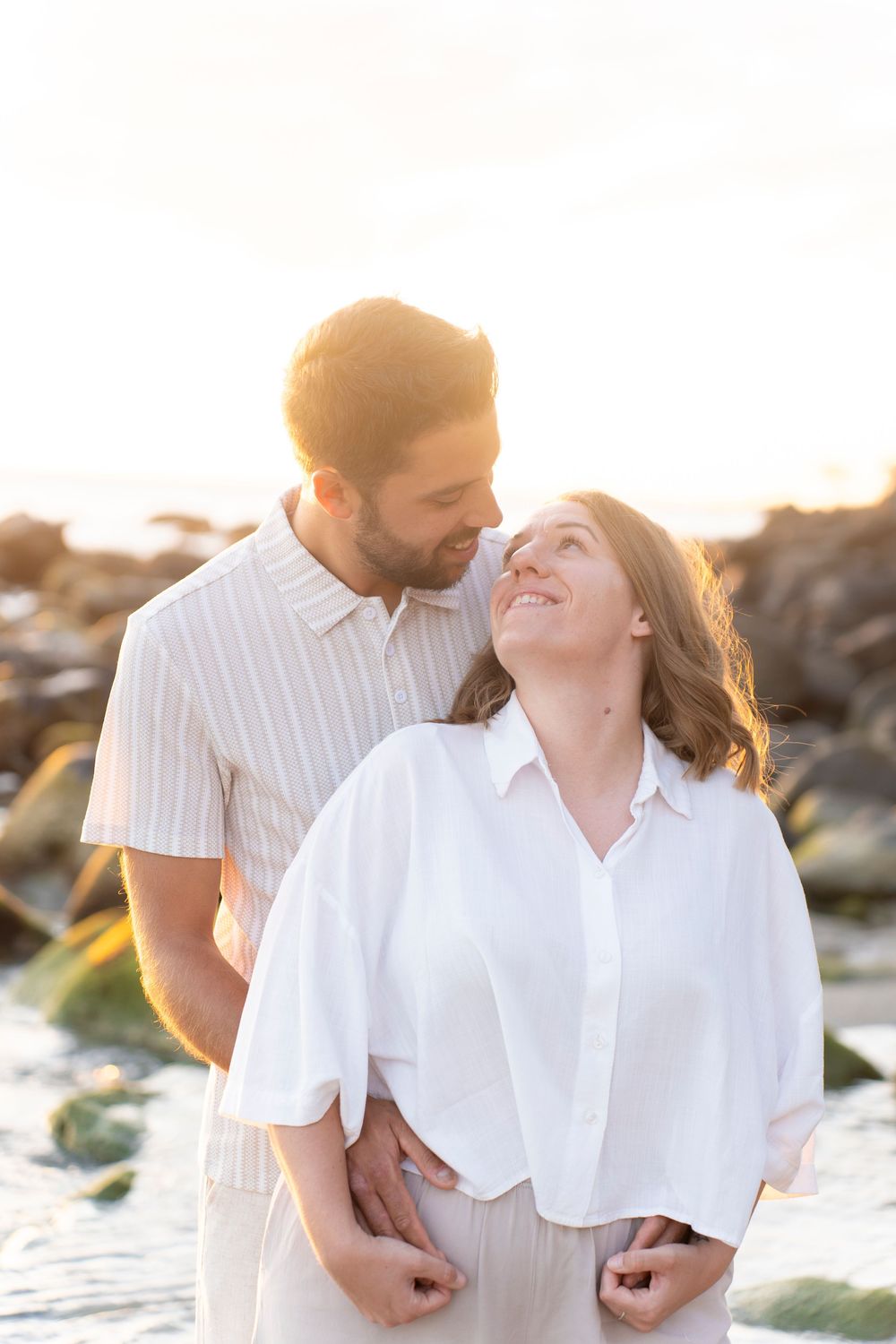 A couple shares a romantic moment on coastal rocks during sunset.
