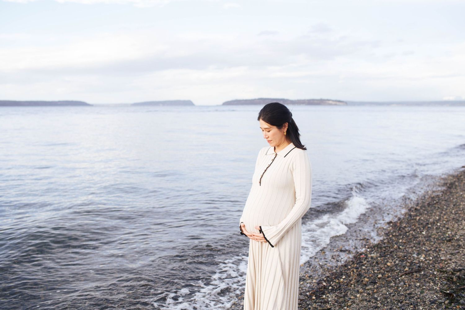 Relaxed intimate motherhood photographer in Seattle WA area: A pregnant mom stands along the beach during a maternity photoshoot