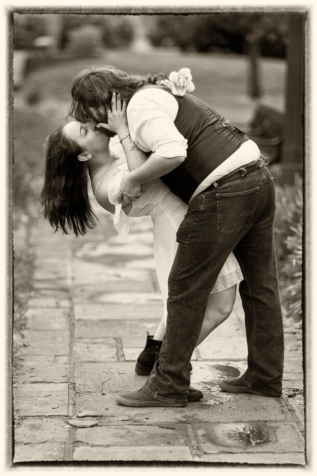 A romantic black and white photograph of a couple sharing an intimate moment on a stone path outdoors.