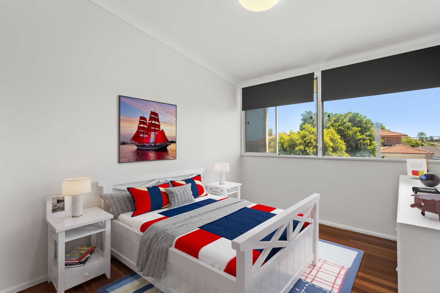 Child's bedroom with white timber bed, nautical artwork, timber floors, and natural light from large window.