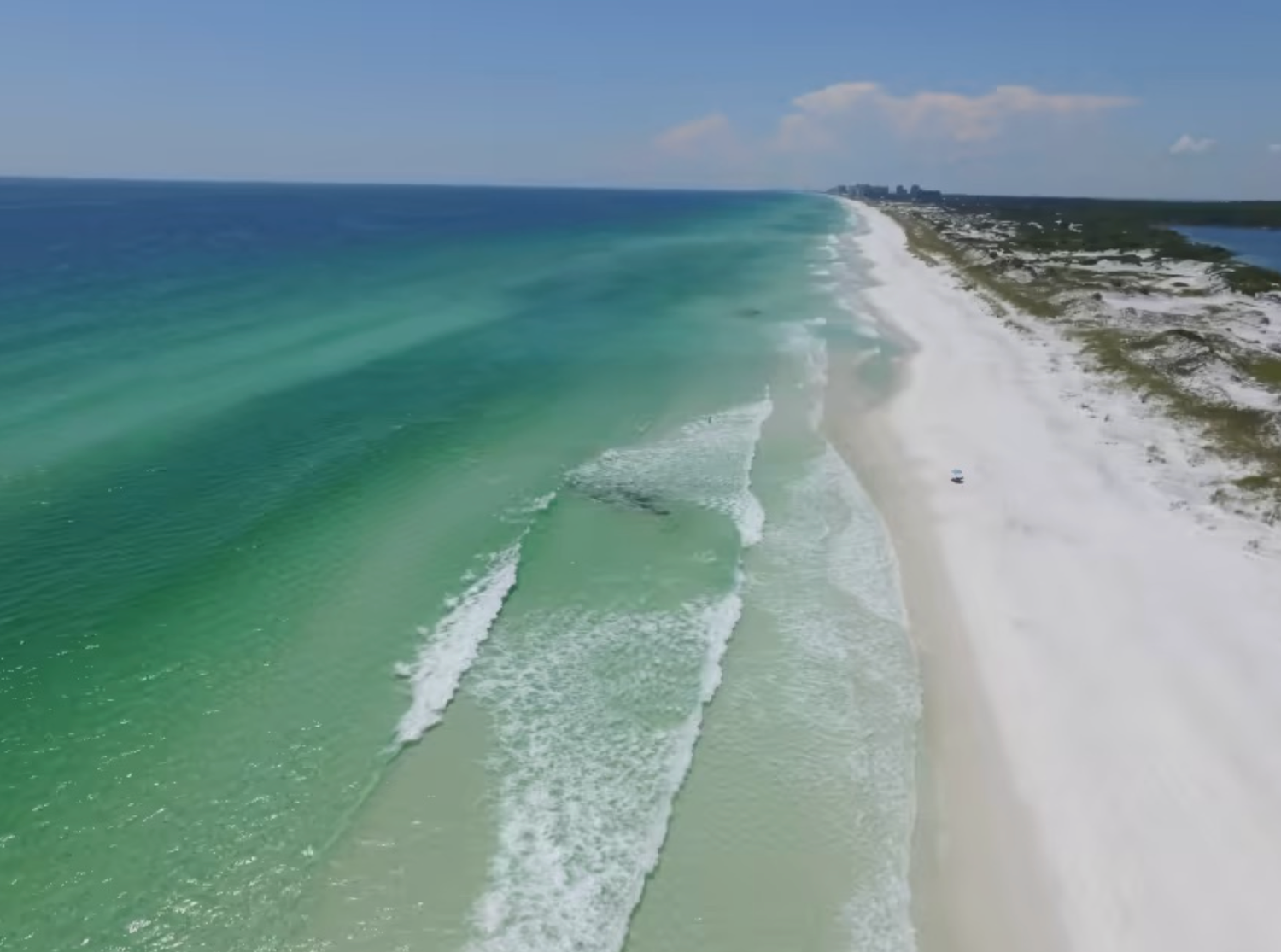 Aerial view of emerald green waves rolling onto pristine white sand beach along Florida's Gulf Coast.