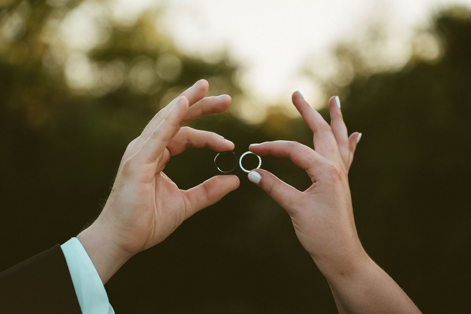 Two hands hold up a wedding ring against a soft blurred outdoor background at sunset. Located in Dayton, Ohio.