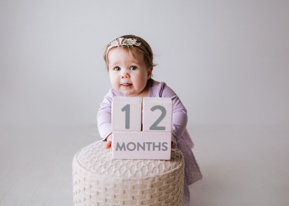 Baby milestone photos with purple number twelve marker against grey background.