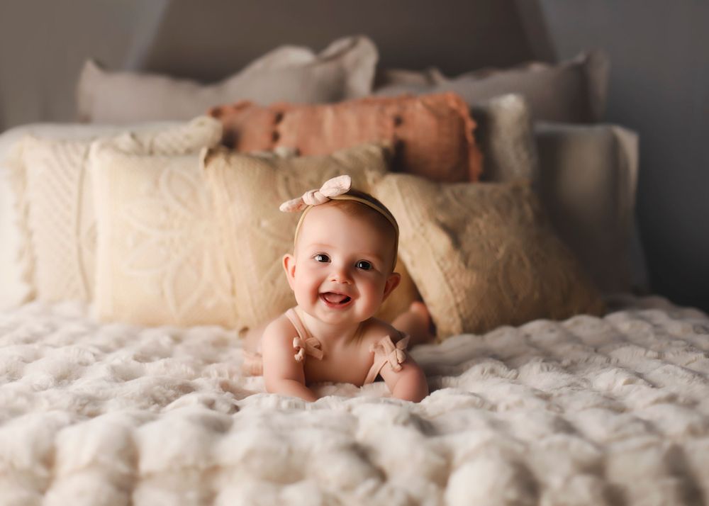 Baby posing on soft white bedding in natural light studio setting.