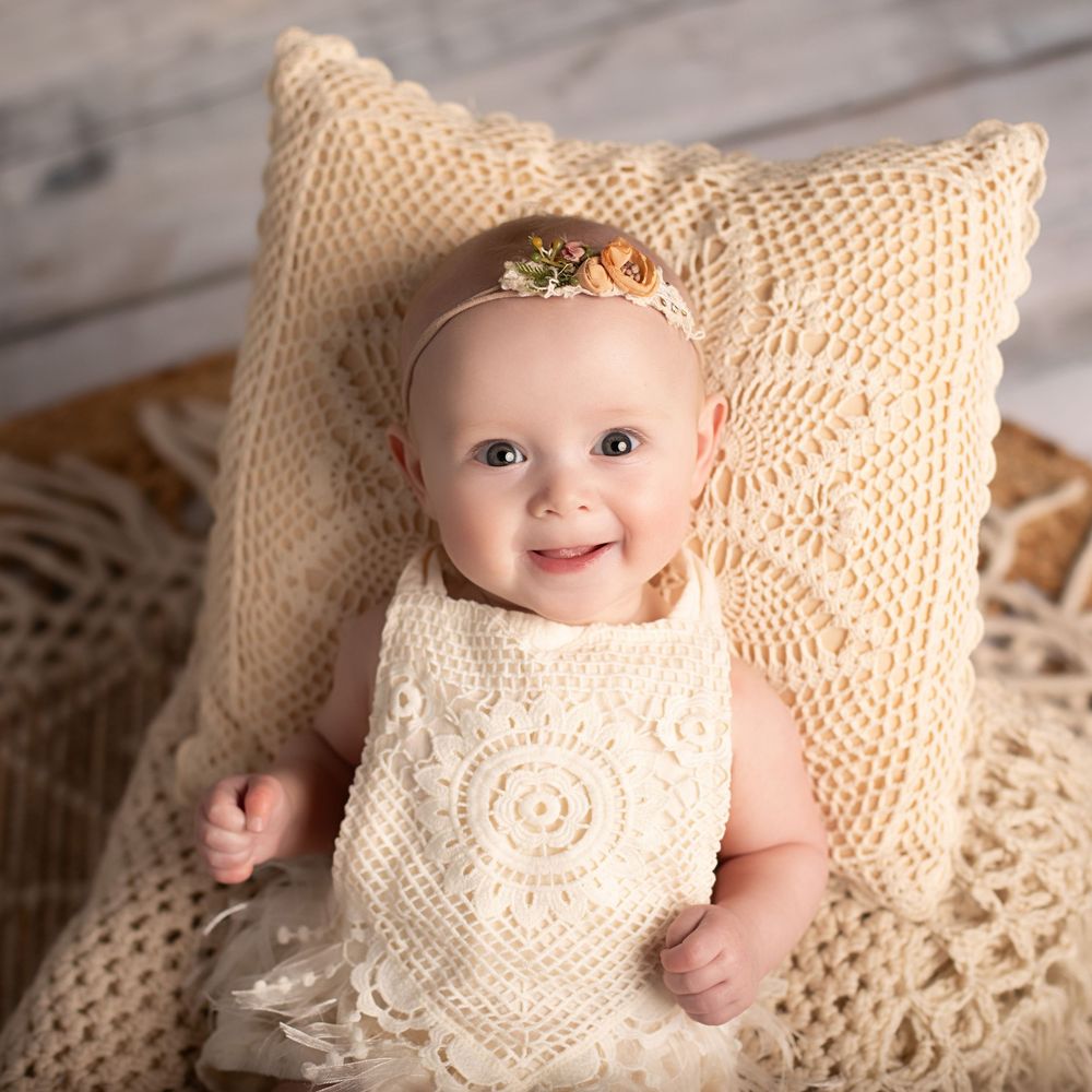 Baby resting on cream lace pillows in delicate vintage-inspired photo series.