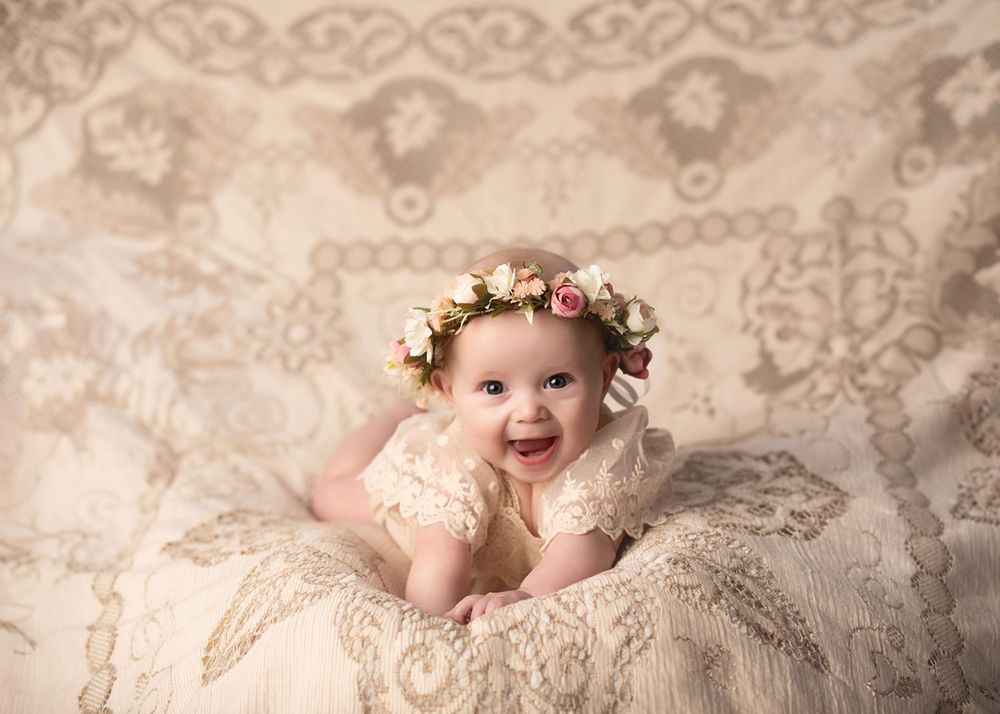 Baby wearing floral crown lies on delicate lace fabric in soft vintage-style portrait photography.