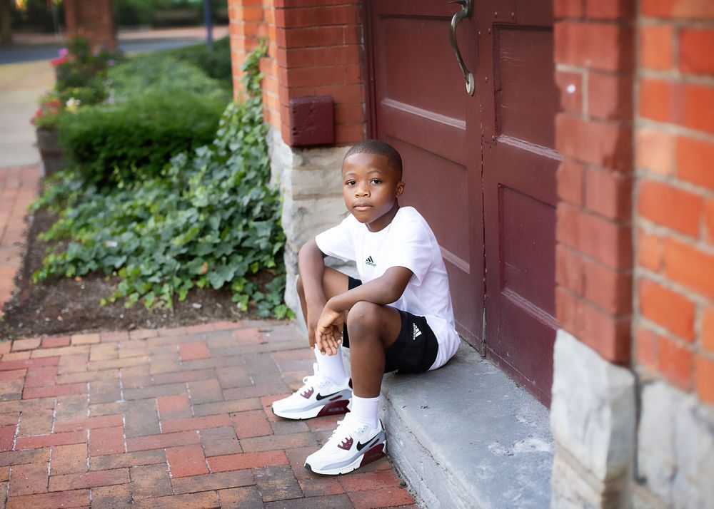 A boy sitting on brick steps in white sneakers downtown.