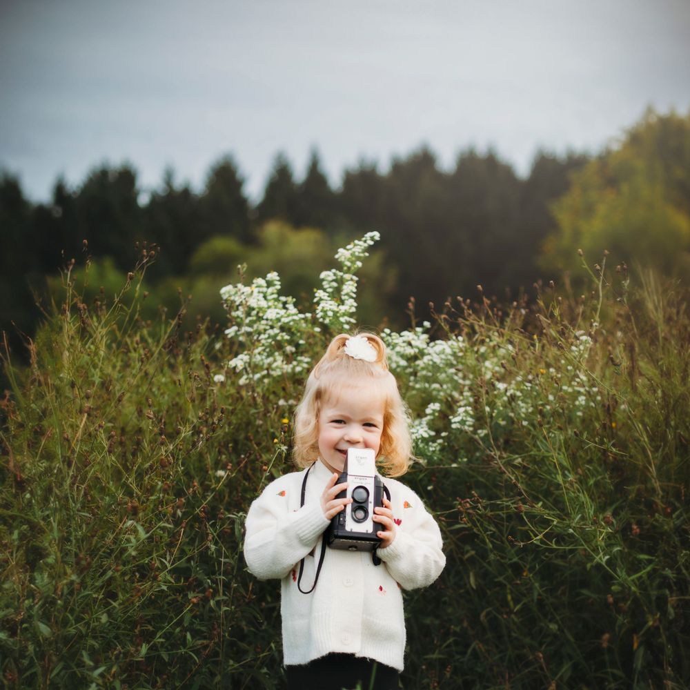 Child in white sweater photographed in field of wildflowers during golden hour.