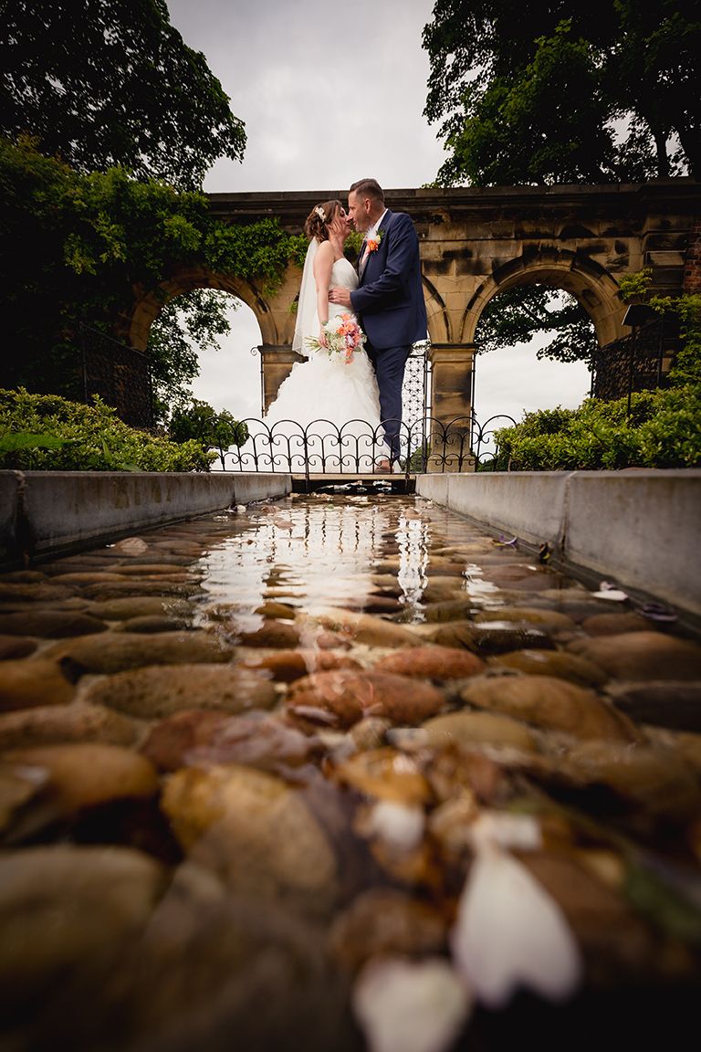 A romantic couple shares an intimate moment on a stone terrace with wrought iron railings at sunset.