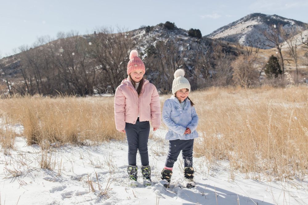 People enjoying a snowy winter day in front of mountain landscape with dry grass visible.