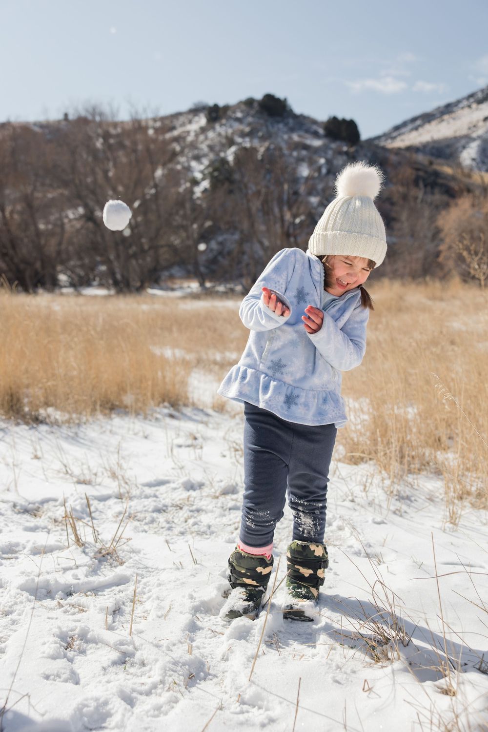 Person in winter clothing bending down to play in fresh snow with mountains in background.