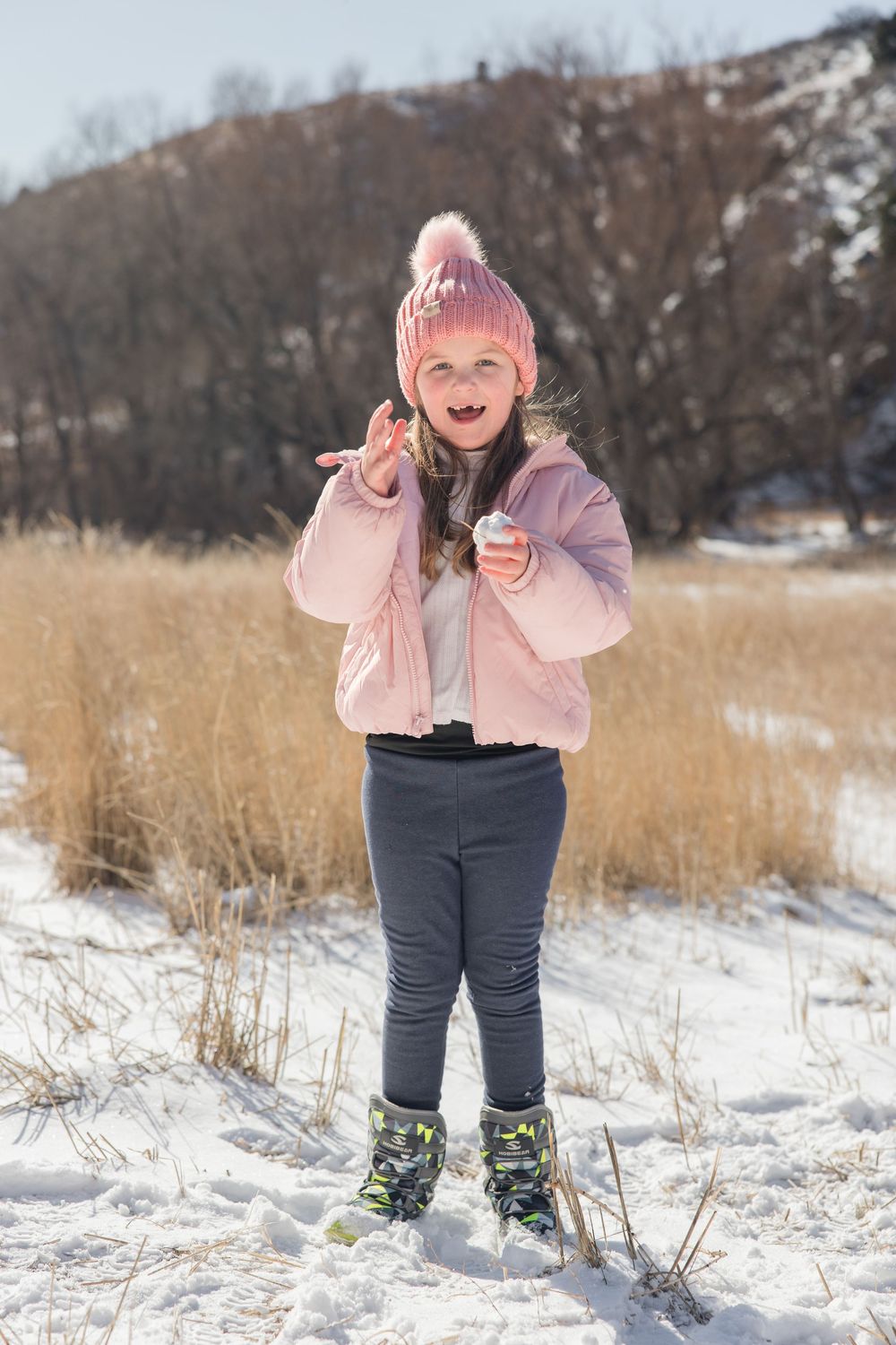Child in pink winter coat and navy pants playing in the snow during a winter photoshoot.