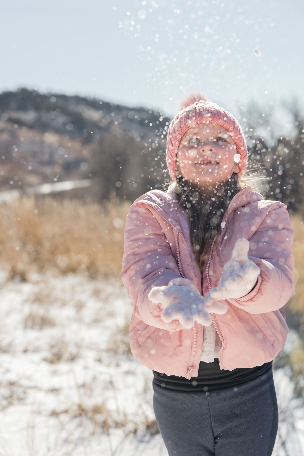 Person in pink coat throwing snow in the air creating a playful winter moment.