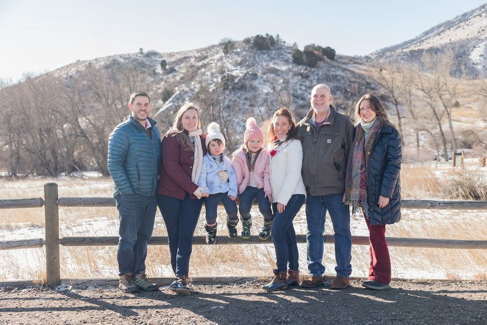 Extended family gathering outdoors against a scenic winter mountain backdrop with wooden fence.