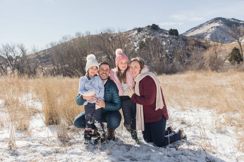 A group poses together on snowy ground with mountains and dry grass in the background.