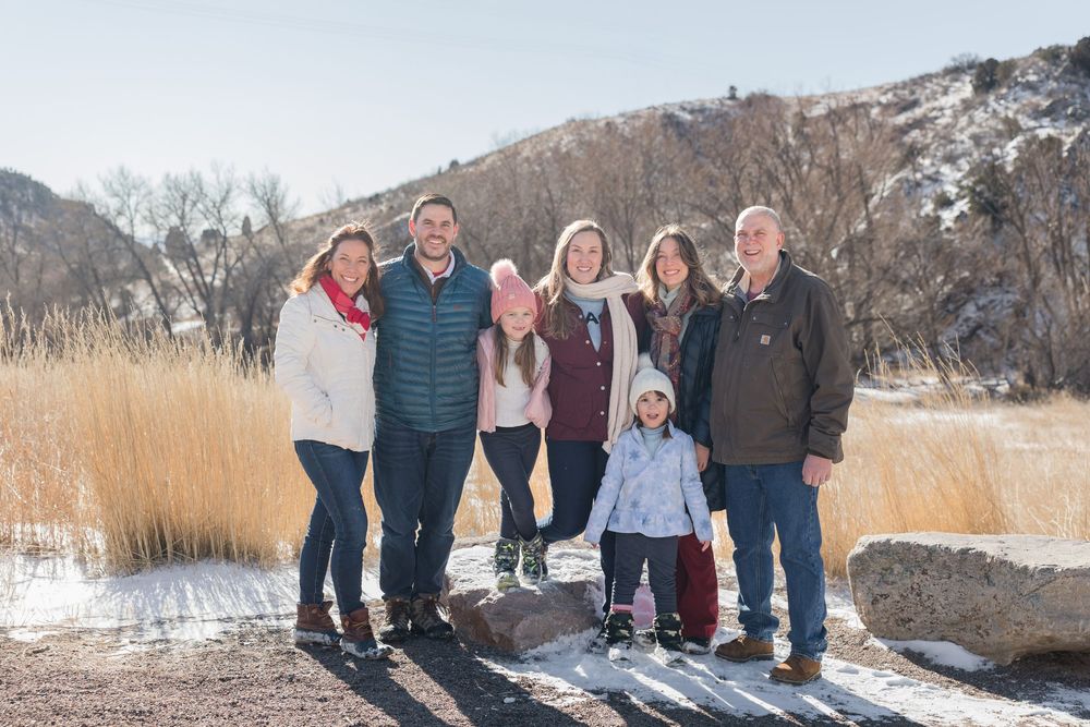 Family photo session in a snowy winter landscape with mountains and dry grass in the background.