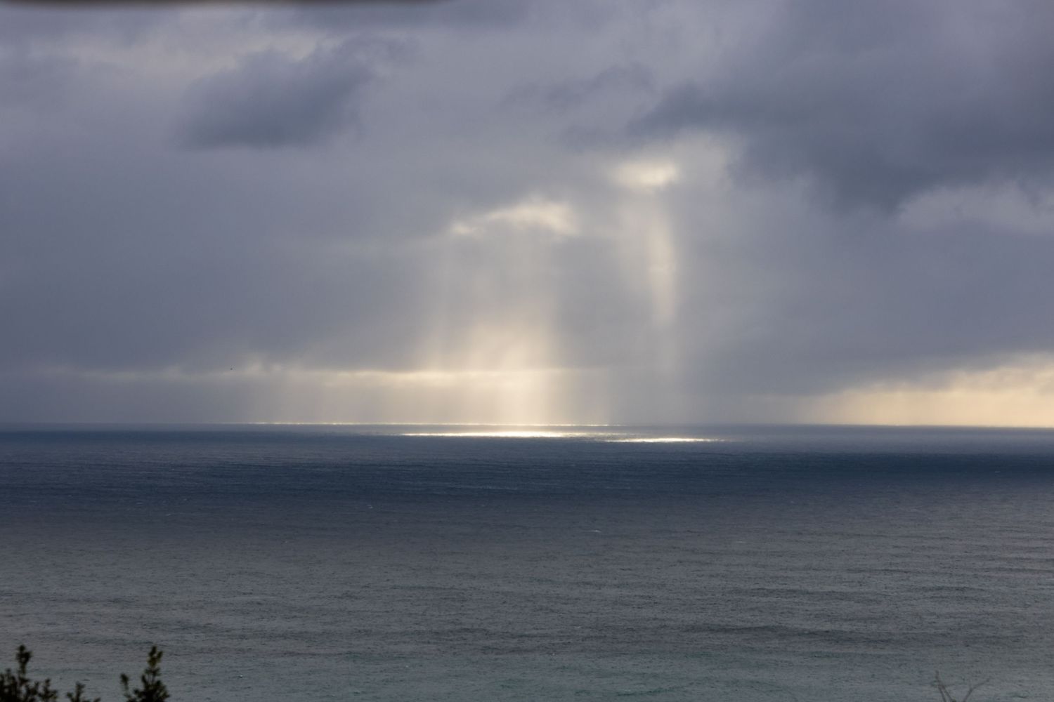 Dramatic sun rays pierce through stormy clouds over a dark ocean creating ethereal light beams on the water's surface.