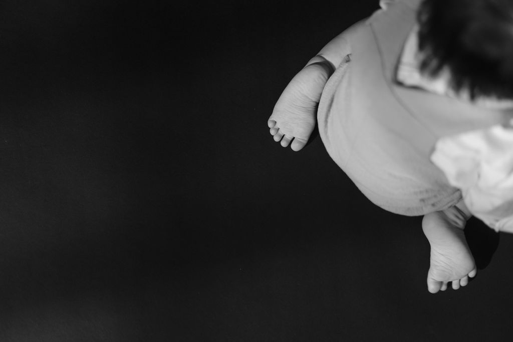 Black and white close-up photo of a newborn baby's tiny feet and chubby legs held gently in the air一張黑白特寫照片，照片中新生兒的小腳丫和胖胖的小腿被輕輕地舉在空中。