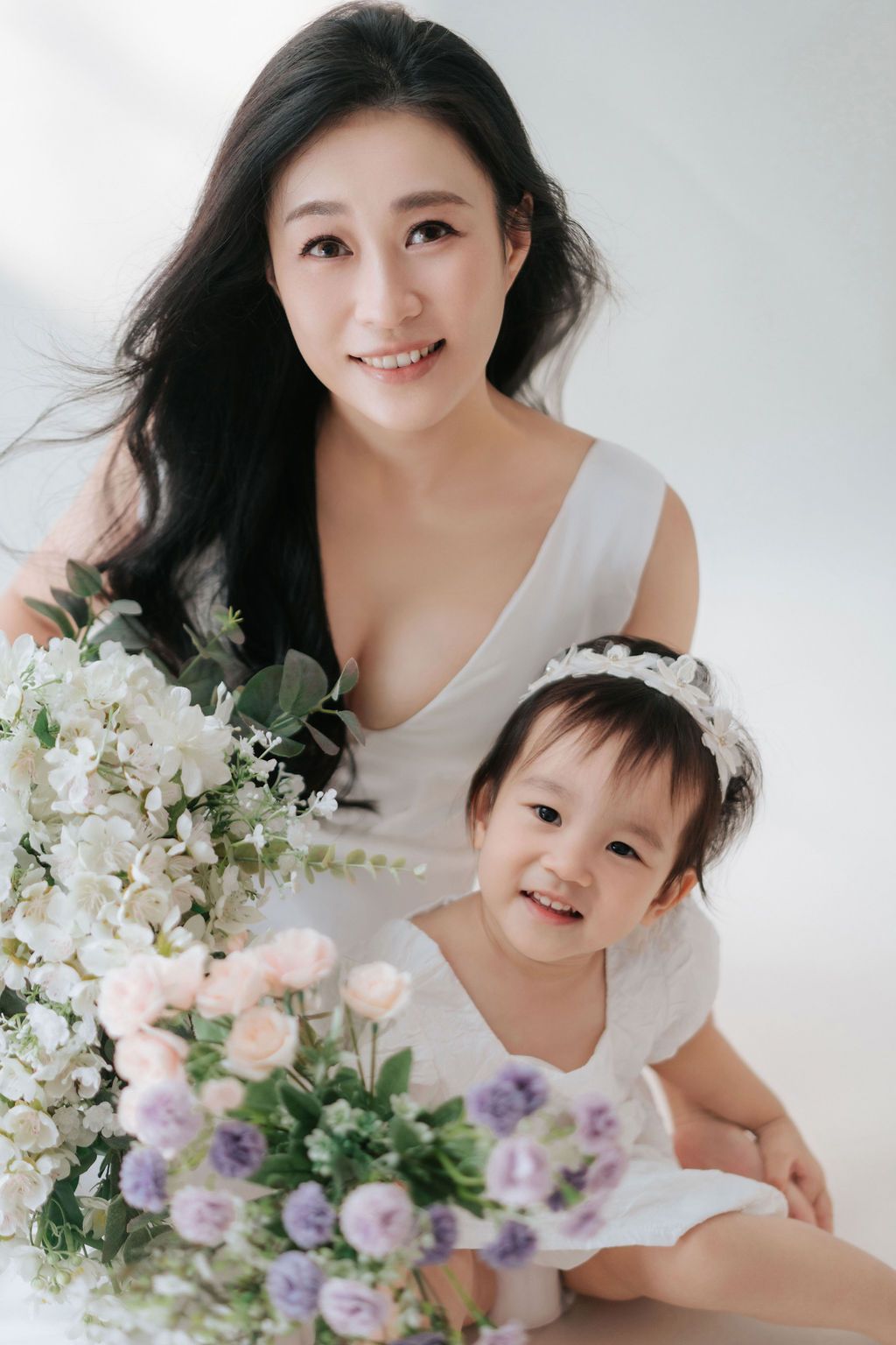 A baby sits in a white chair surrounded by floral decorations and balloons at a birthday celebration.在生日慶祝活動中，一個嬰兒坐在白色椅子上，周圍環繞著鮮花裝飾和氣球。