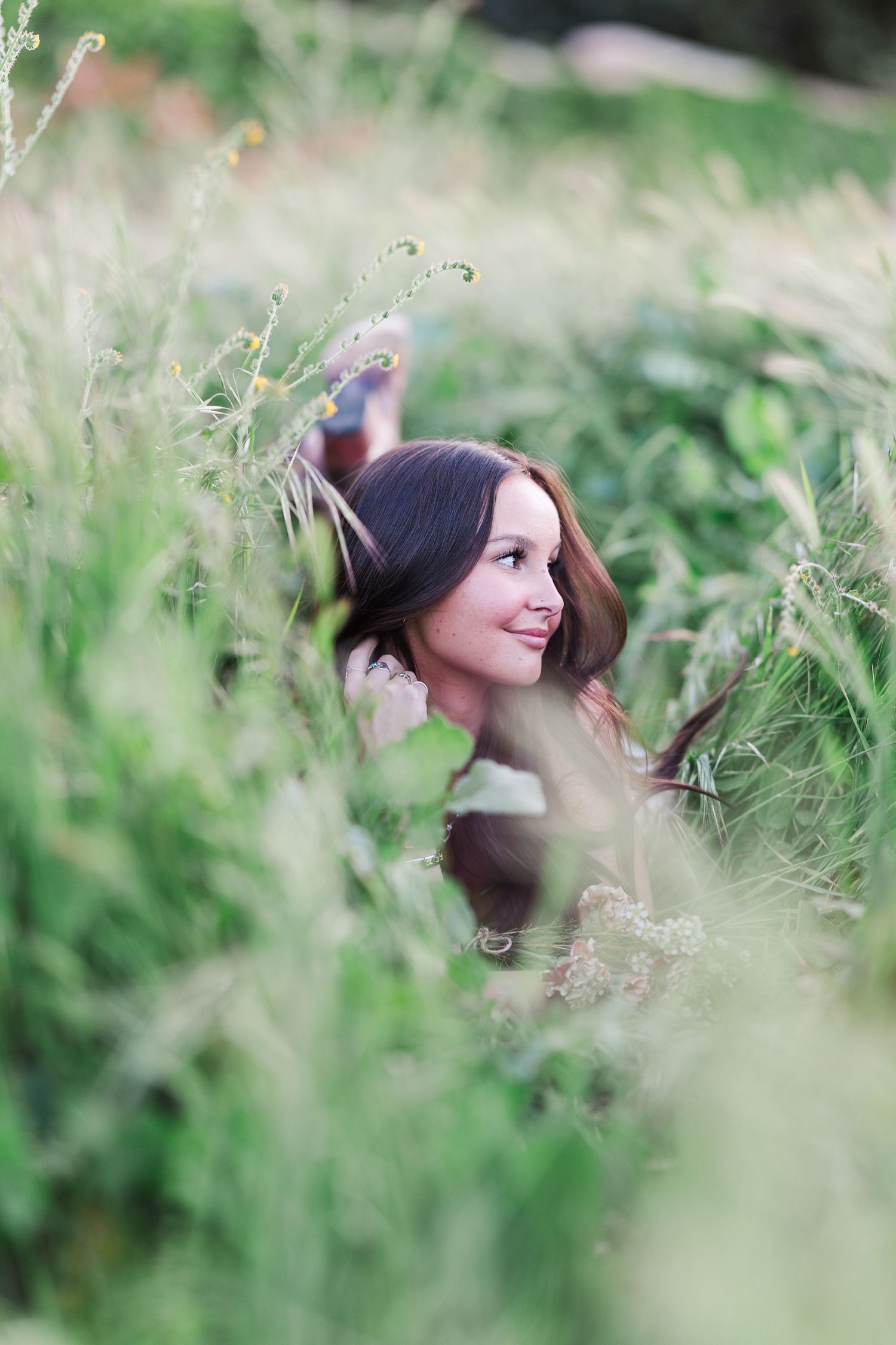 A series of photos showing someone in a dark sweater peeking through tall grass and wildflowers in a natural outdoor setting.