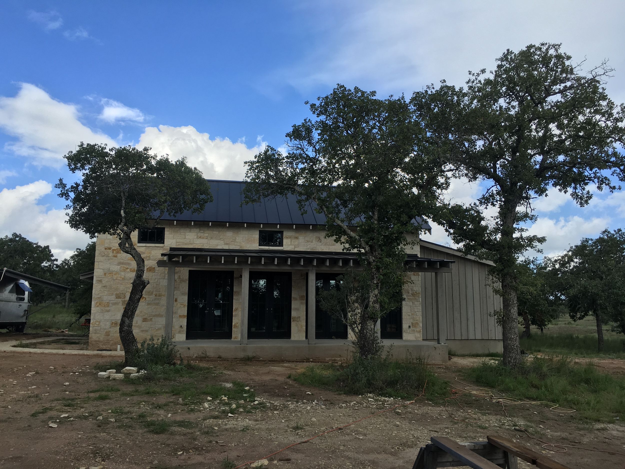 Panoramic view of a rustic stone and wood house construction site in a rural Texas setting.