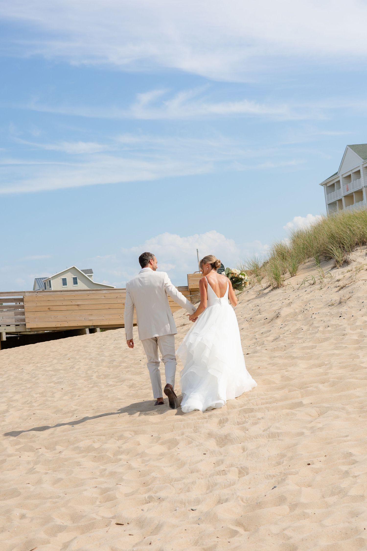 Bride and groom sharing a romantic kiss under a flowing veil in golden sunset light, with a bouquet of white and purple flowers.