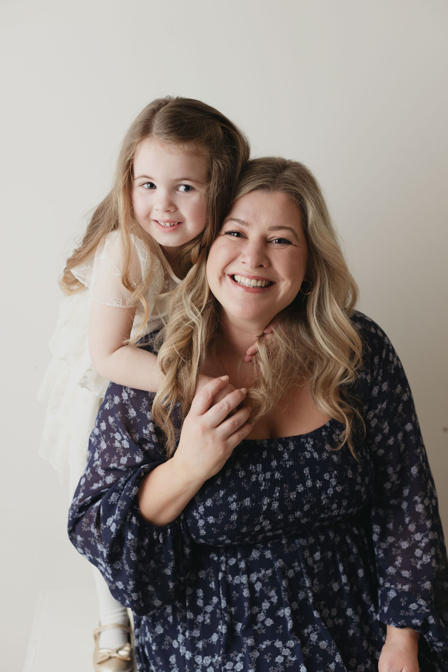 A joyful portrait of two people embracing and smiling against a light gray background.