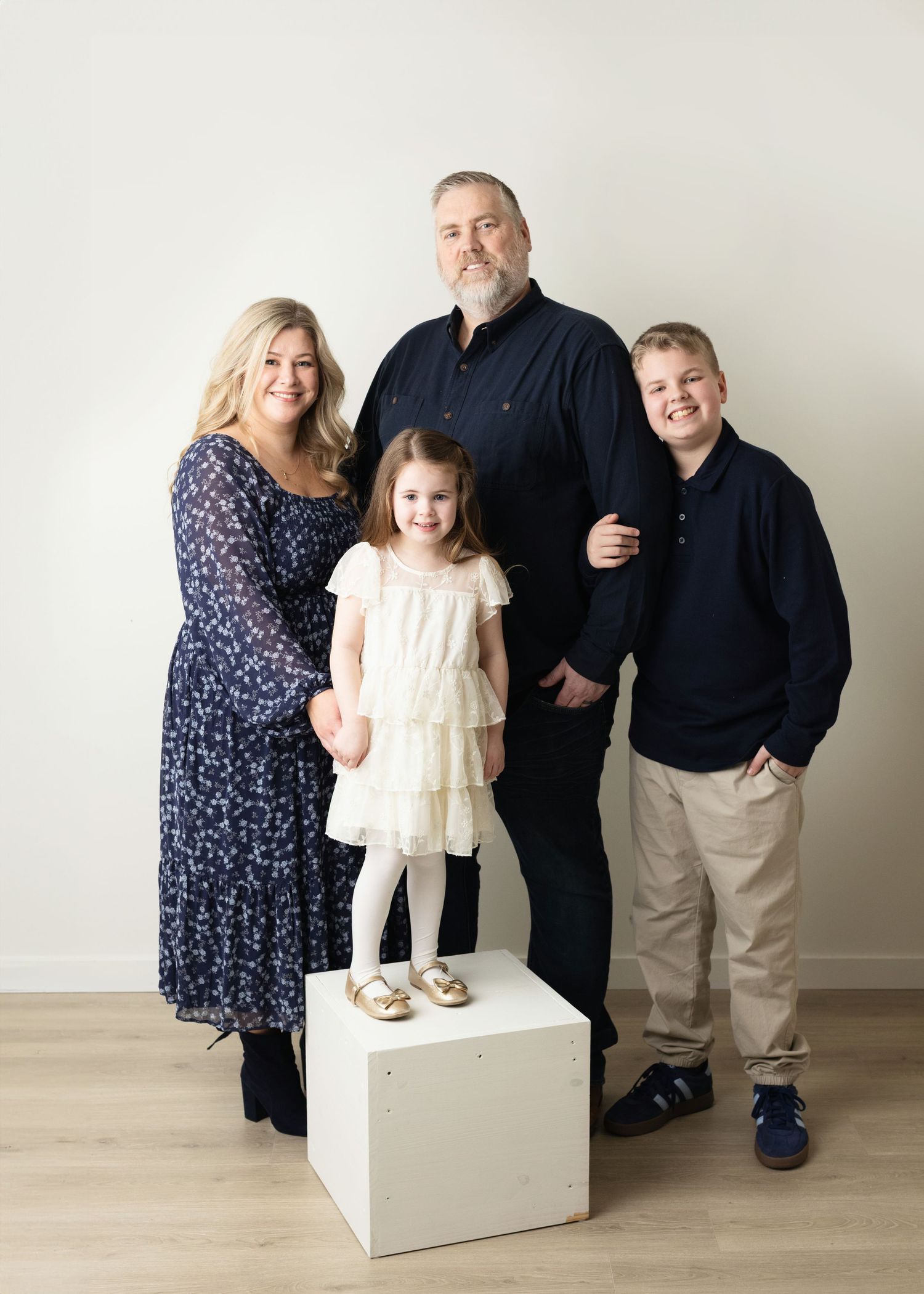 A family poses together in a studio setting wearing coordinated outfits of navy and white against a neutral background.