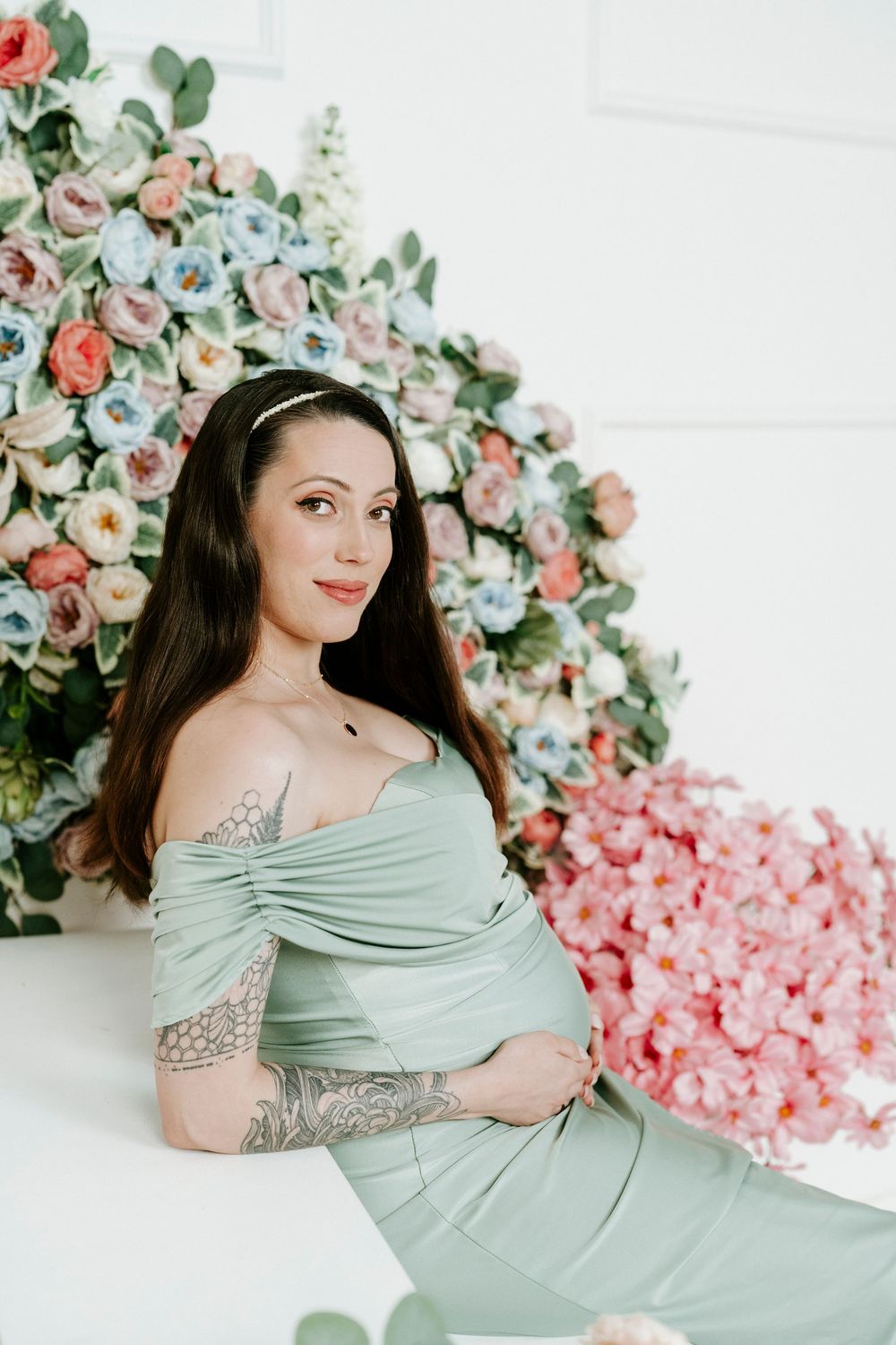 Maternity photoshoot with soft sage green dress against floral backdrop of pink and peach roses.