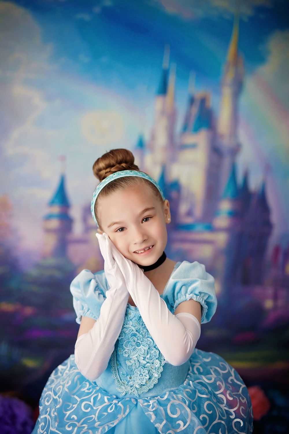 A child in a blue princess dress poses playfully against a dreamy castle backdrop in a magical portrait session.