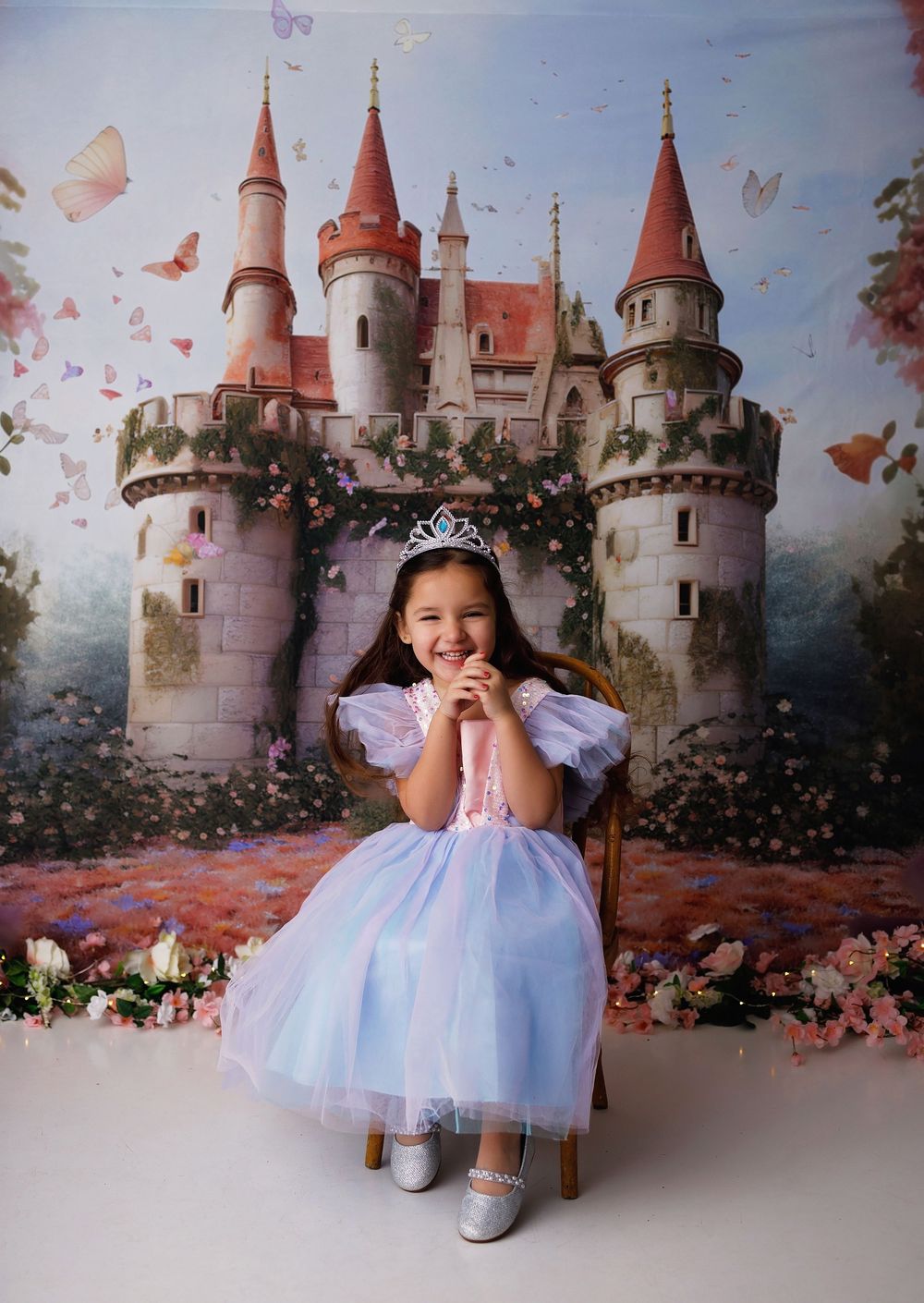 A dreamy princess-themed photo setup with a fairytale castle backdrop decorated with flowers and butterflies.