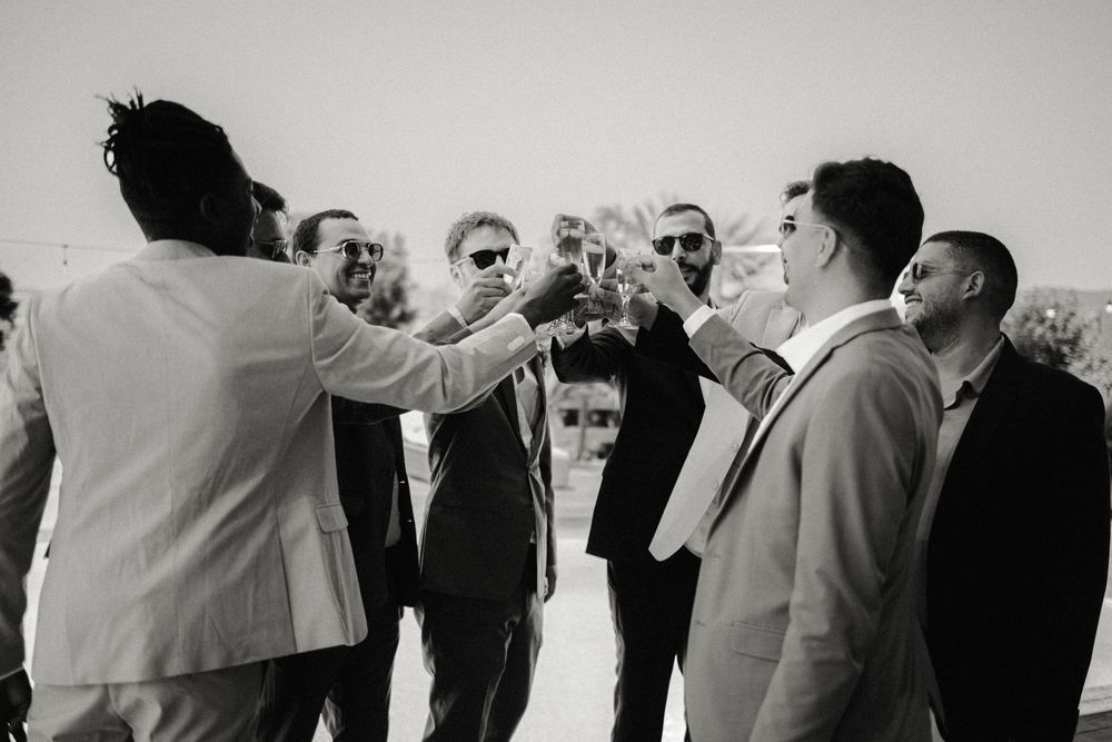 A group of wedding guests in formal attire standing in a line against a white background.